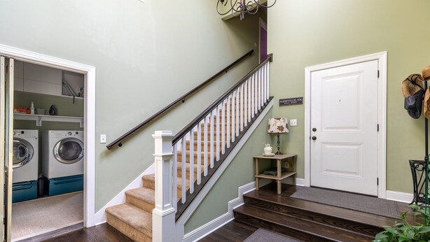 A staircase with a wooden handrail and beige carpeted steps leading to a landing with a white door and a small table with a lamp. - Easy access to Taylor Swift, Broadway, CMAs & more (Nashville)