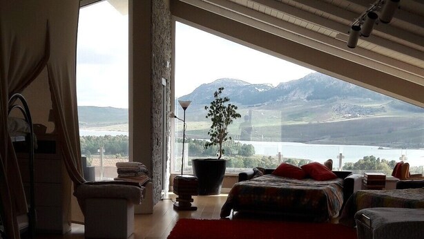 A spacious room with a large bed, a potted plant, and a view of mountains and a lake. - escape escape from palermo (Piana degli Albanesi)