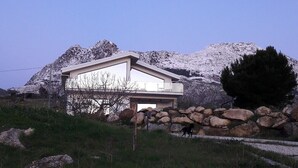 A modern house with a flat roof, large windows, and a balcony. It is surrounded by a grassy area with large rocks and a mountain in the background. - escape escape from palermo (Piana degli Albanesi)