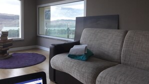 A living room with a sofa, a window with a view of a lake and mountains, a purple rug, and a tablet on the floor. - escape escape from palermo (Piana degli Albanesi)