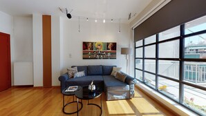Ein modernes Wohnzimmer mit einem Ecksofa, einem kleinen Couchtisch und einem großen Fenster mit Blick auf die Stadt.