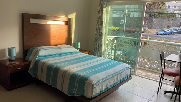 Une chambre d’hôtel avec un lit, des tables de chevet, une table et une vue sur la rue depuis un balcon.
