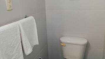 A bathroom with a toilet, a blue mat, a white towel, and a trash bin.