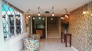 Un hall d’hôtel avec un mur orné de motifs, un comptoir d’accueil, un escalier et une chaise colorée.