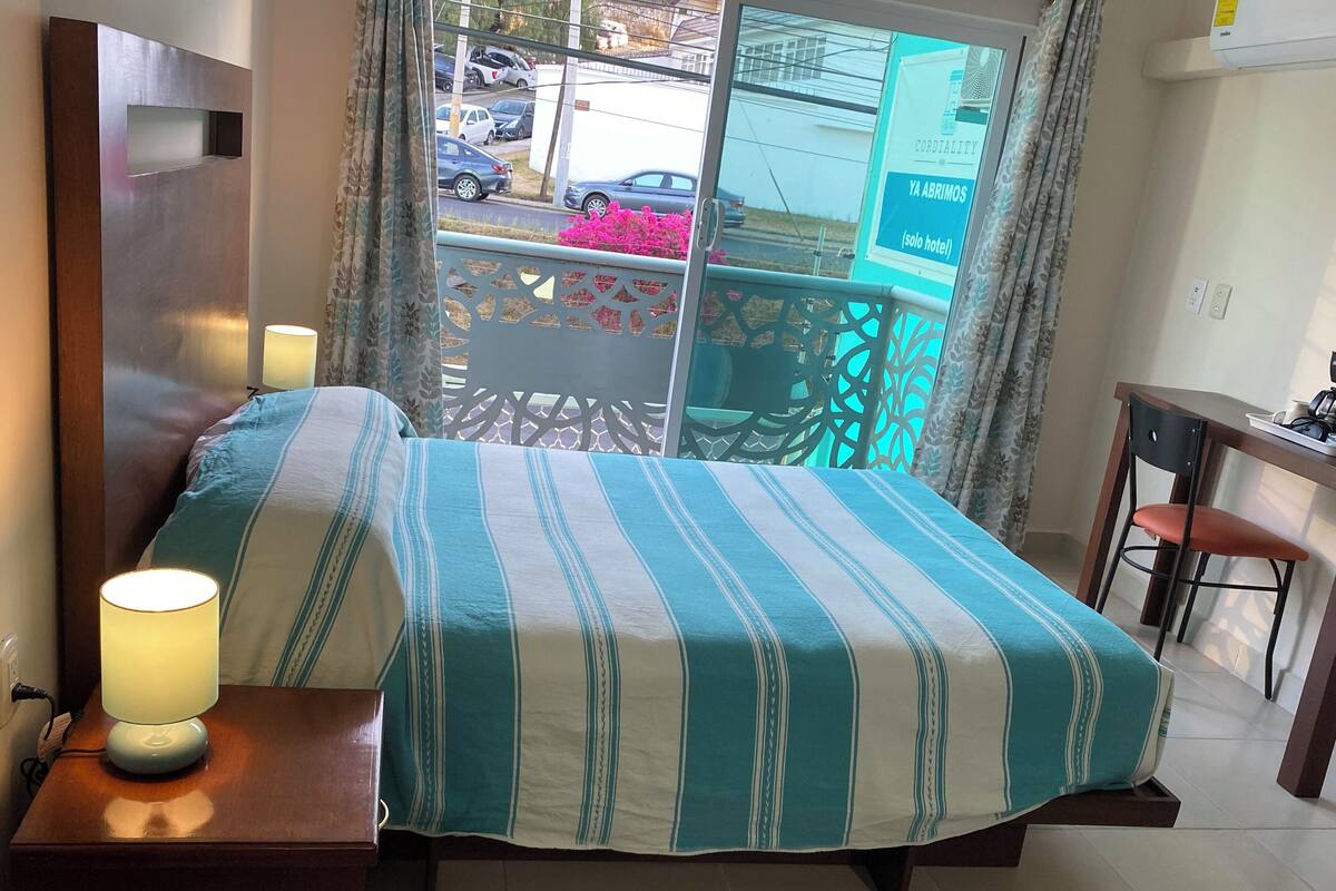 A hotel room with a bed, bedside lamps, a desk, and a chair.