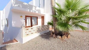 Un bâtiment blanc doté d’un balcon, d’un palmier et d’une allée gravillonnée.