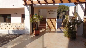 L’entrée d’un immeuble, avec une enseigne indiquant « Apartamentos Colomar », un escalier et des plantes en pot.