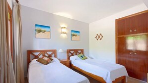 Une chambre avec deux lits simples, une armoire en bois et deux lampes fixées au mur.