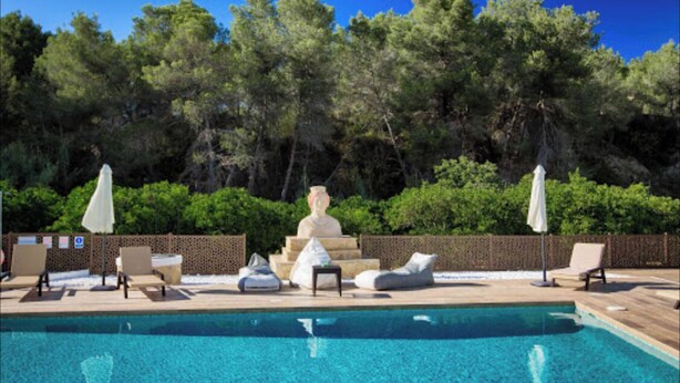 Une piscine entourée d’une terrasse en bois et de nombreux arbres, avec des chaises longues et des parasols à proximité.