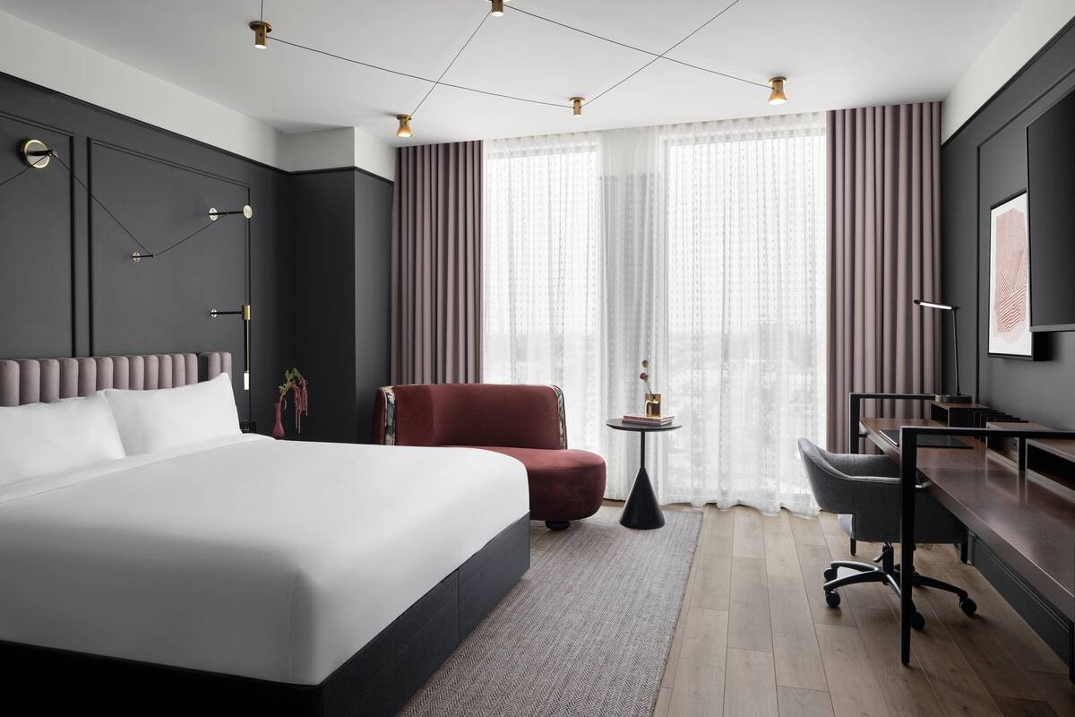 A modern hotel room with a large bed, a desk, and a chair.
