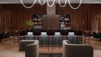 A modern bar area with a central bar, multiple stools, and a decorative light fixture.