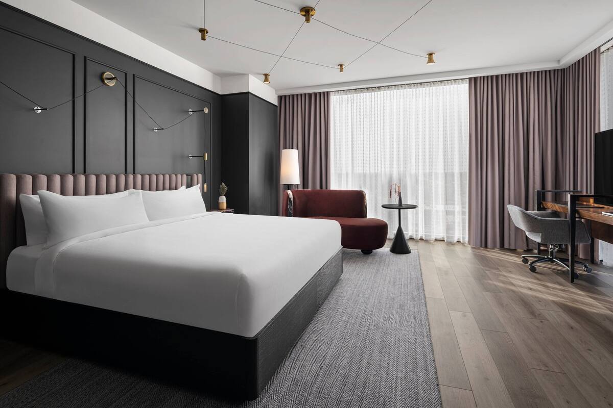 A modern hotel room with a large bed, a desk, a chair, and a TV.