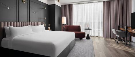 A modern hotel room with a large bed, a desk, a chair, and a TV.