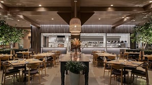 En modern restaurang med träbord och stolar, en stor krukväxt i mitten och en hängande lampa.