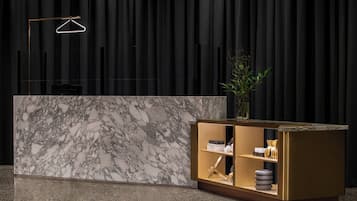 A reception desk with a marble top and a gold base, a hanging light fixture, and a potted plant.