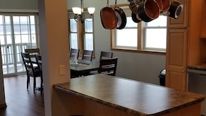A kitchen with a granite countertop, hanging pots, a dishwasher, and a dining area with chairs and a table. - River Life at it's Best (Chillicothe)