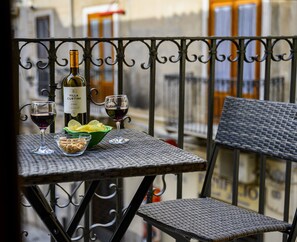 Un balcón con una mesa preparada para dos personas, que incluye una botella de vino Villa Curtini, dos copas, un cuenco de patatas fritas y un cuenco de nueces.