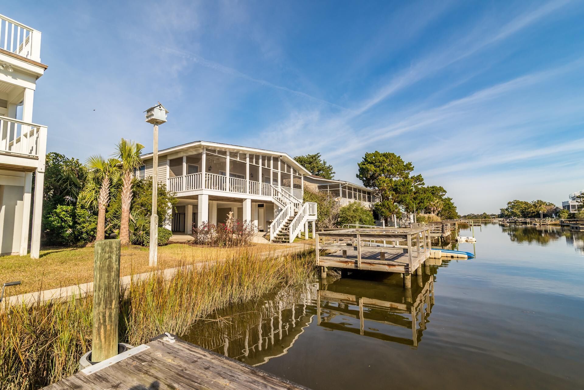 A waterfront property with a large house featuring a covered porch and a dock extending into a calm body of water.