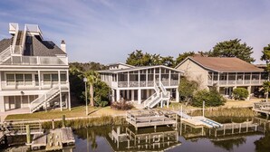 Een pand aan het water met meerdere gebouwen, waaronder een groot huis met balkon en een kleinere constructie met overdekte veranda.