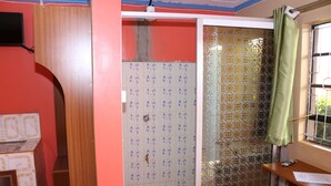 A bathroom with a red wall, a tiled shower area, and a window with a curtain.