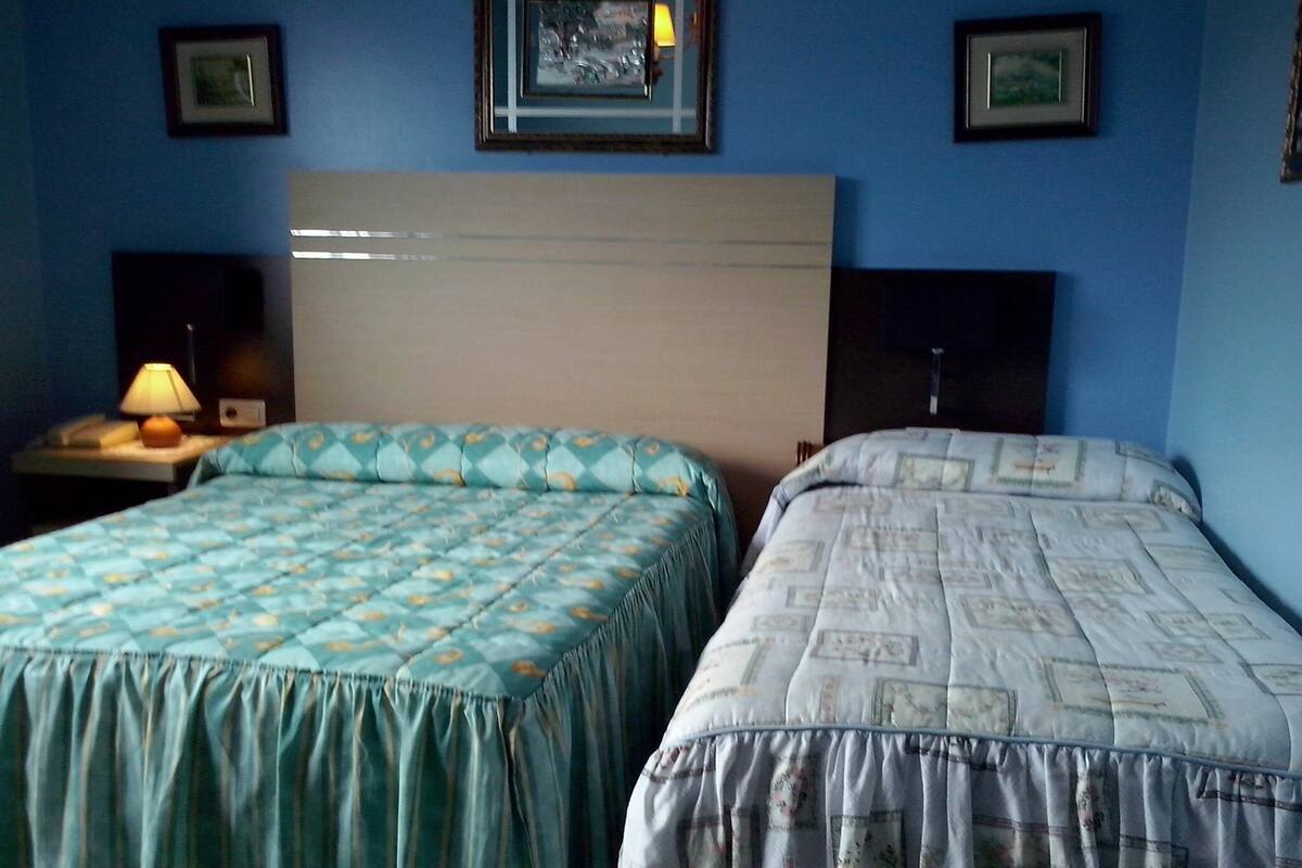 A hotel room with two beds, a nightstand with a lamp, and framed pictures on the wall.