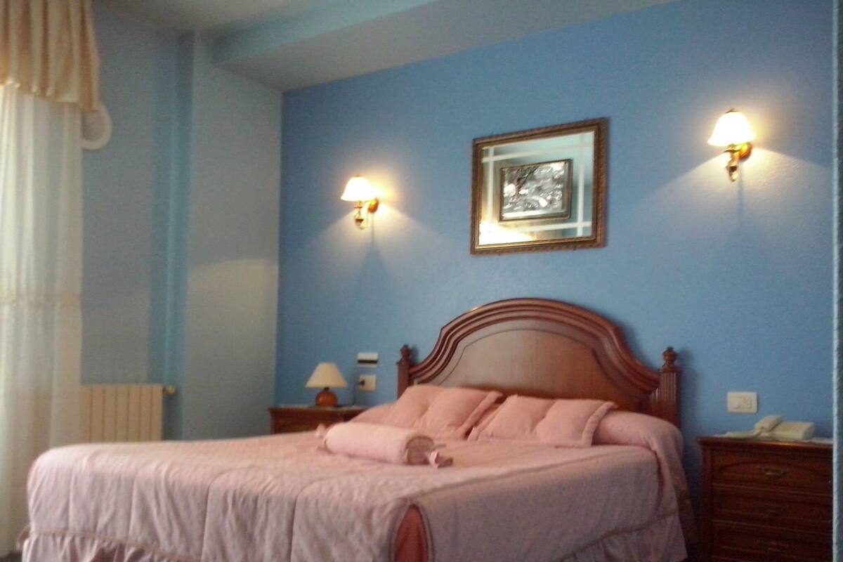 A bedroom with a single bed, a nightstand, a lamp, and a wall-mounted light fixture.