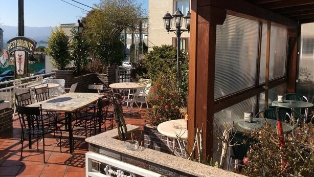 An outdoor patio area with tables and chairs, a wooden pergola, and a view of the cityscape. - Hotel Internacional (O Porrino)