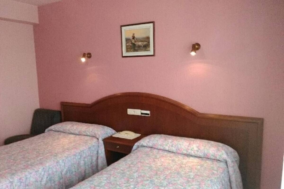 A hotel room with two single beds, a wooden headboard, a nightstand, and a wall-mounted picture.