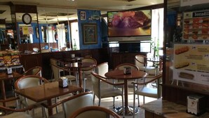 A restaurant interior with multiple tables and chairs, a television mounted on the wall, and a menu board on the right. - Hotel Internacional (O Porrino)