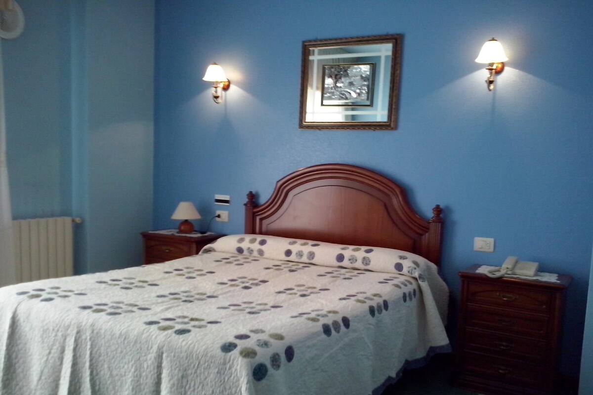 A bedroom with a wooden bed, two bedside tables with lamps, a framed picture on the wall, and a radiator.