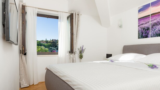 A bedroom with a large bed, a window with curtains, a potted plant, and a painting on the wall. - Spalato Dream Apartments (Split)