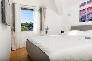 A bedroom with a large bed, a window with curtains, a potted plant, and a painting on the wall. - Spalato Dream Apartments (Split)