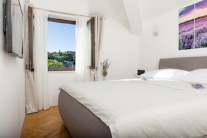 Une chambre à coucher avec un grand lit, une fenêtre avec des rideaux, une plante en pot et un tableau accroché au mur.