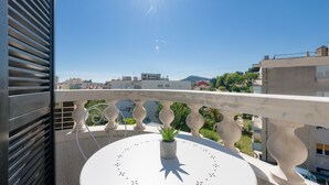 A balcony with a potted plant, a white table, and a clear view of the surrounding buildings and landscape. - Spalato Dream Apartments (Split)