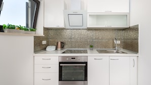 A modern kitchen with white cabinets, a built-in oven, a stainless steel sink, and a window with plants on the countertop. - Spalato Dream Apartments (Split)