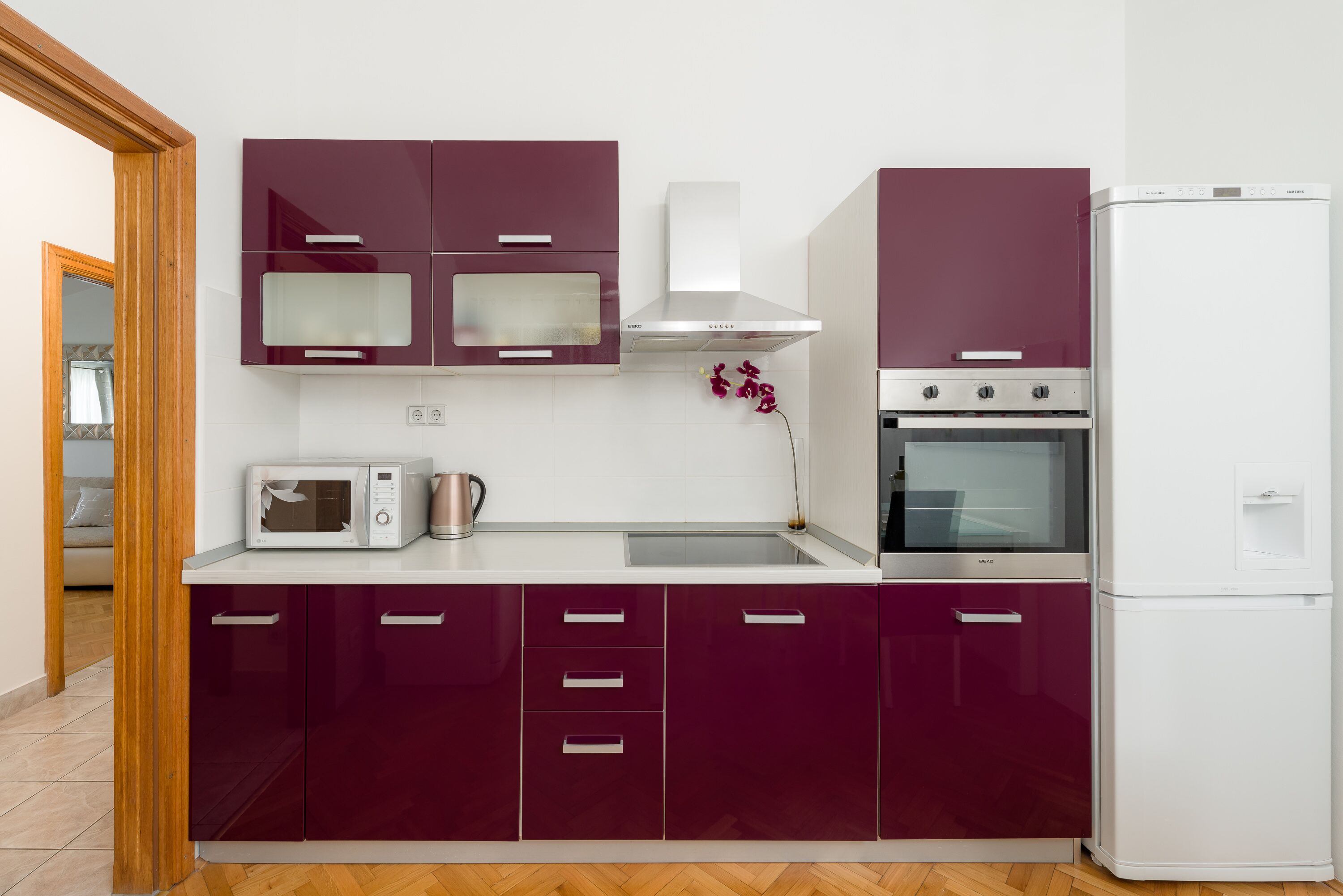 A modern kitchen with purple cabinets, a microwave, a kettle, and a built-in oven.