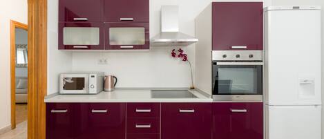 A modern kitchen with purple cabinets, a microwave, a kettle, and a built-in oven.