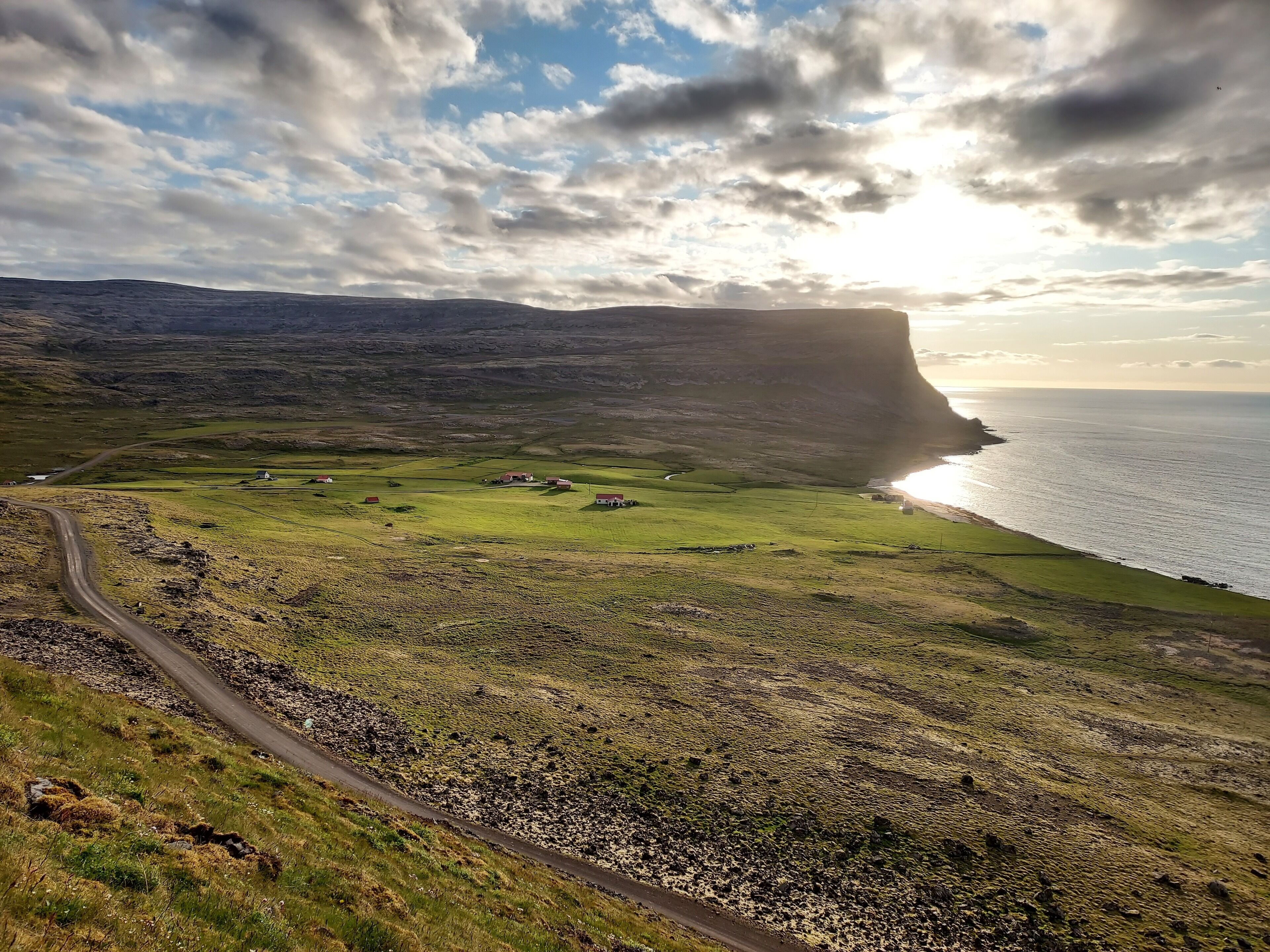 A coastal landscape with a prominent cliff, a winding road, and scattered buildings.