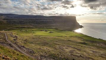A coastal landscape with a prominent cliff, a winding road, and scattered buildings.