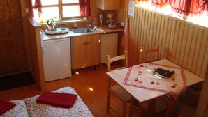 Una cocina compacta con pileta, cafetera y heladera pequeña. Hay una mesa de comedor con mantel rojo y una silla.