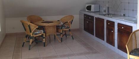 A compact kitchen with a dining area, featuring a round table, wicker chairs, a microwave, and a tiled backsplash.