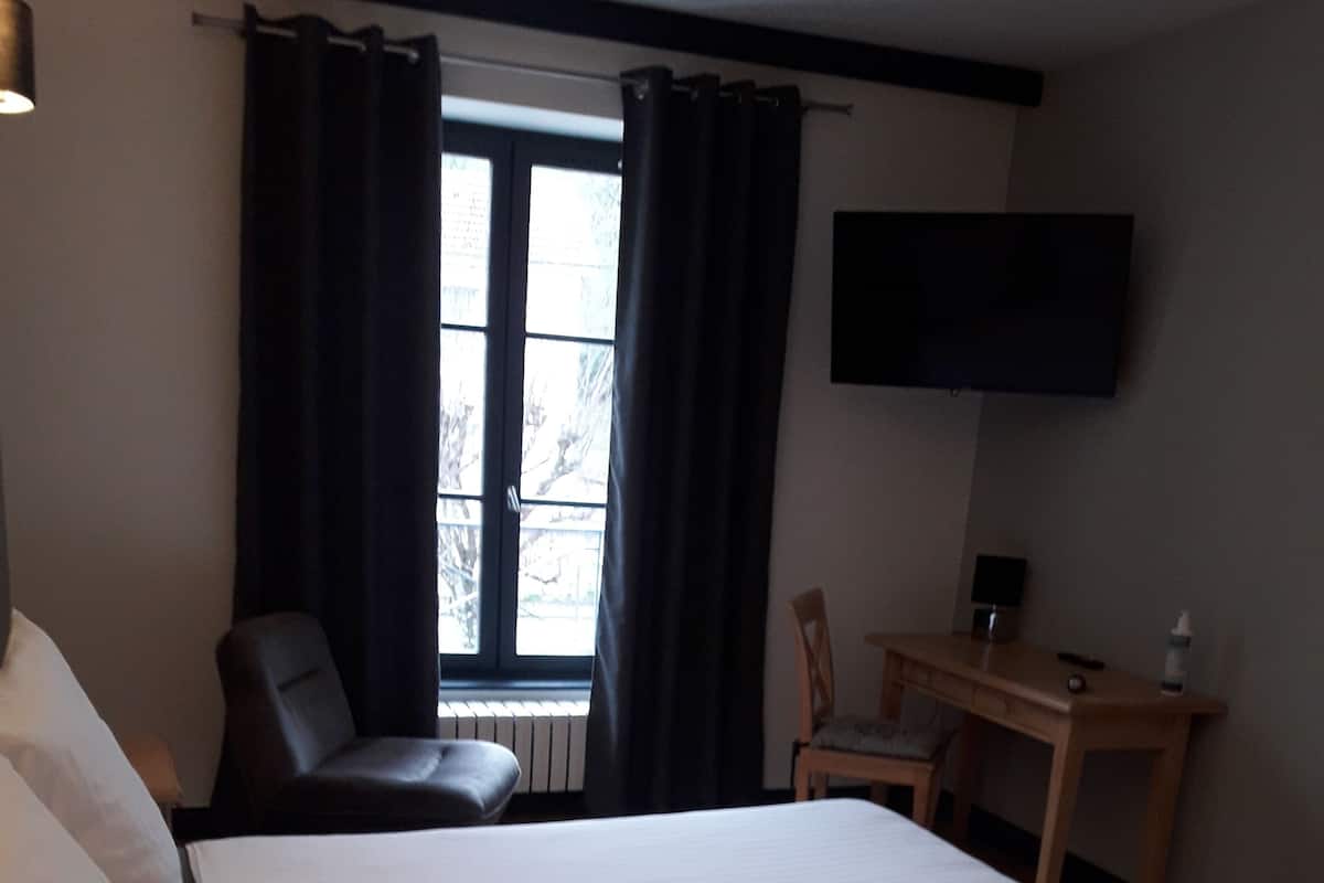 A hotel room with a bed, a desk, a chair, a TV, and a window with curtains.