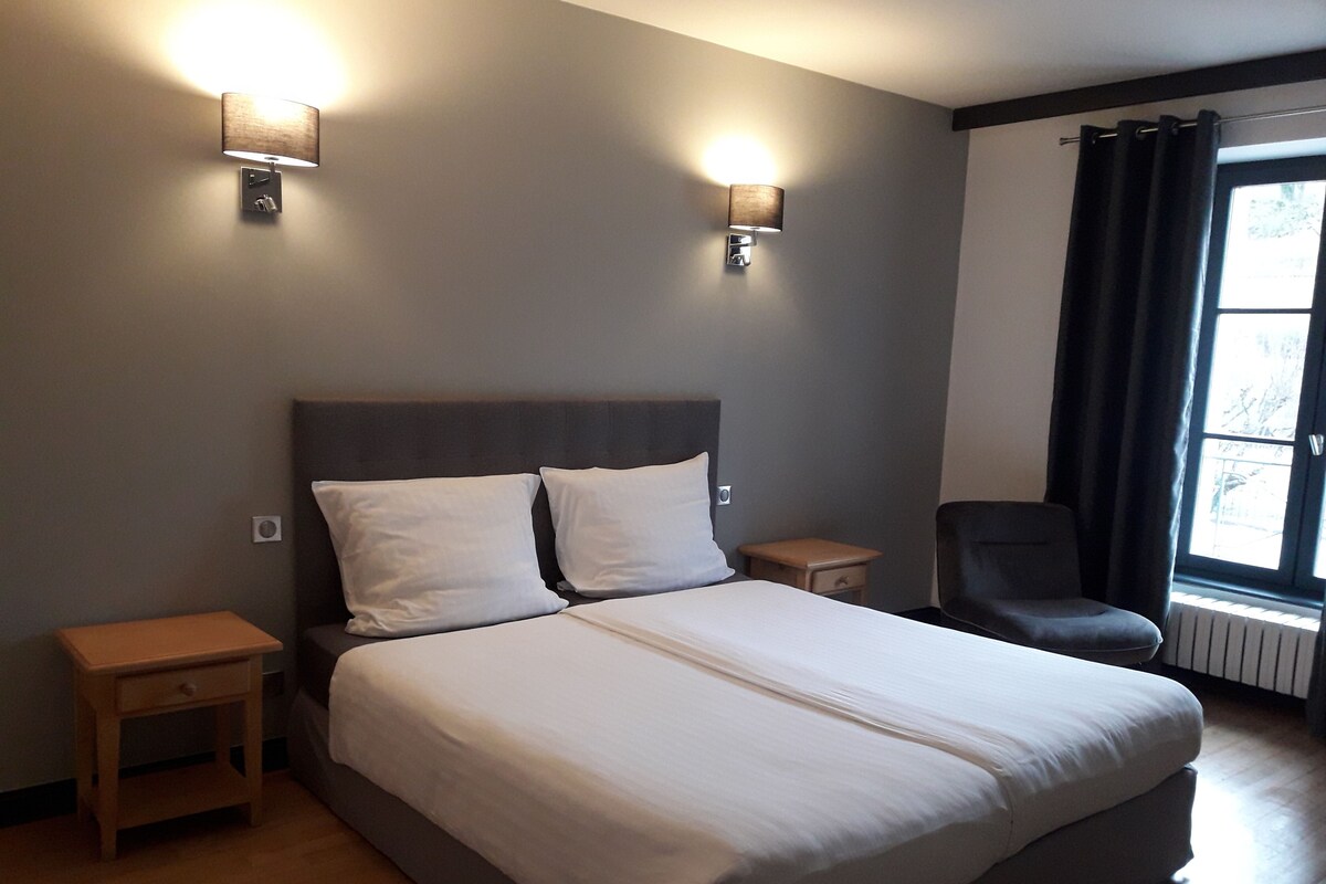 Una habitación de hotel con una cama grande, dos mesitas de noche, una silla y dos lámparas de pared.