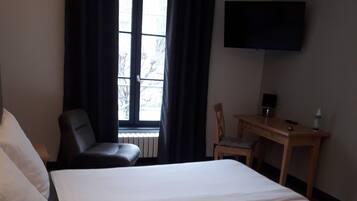 Habitación de hotel con una cama grande, un escritorio, una silla, un televisor montado en la pared y una ventana con cortinas.