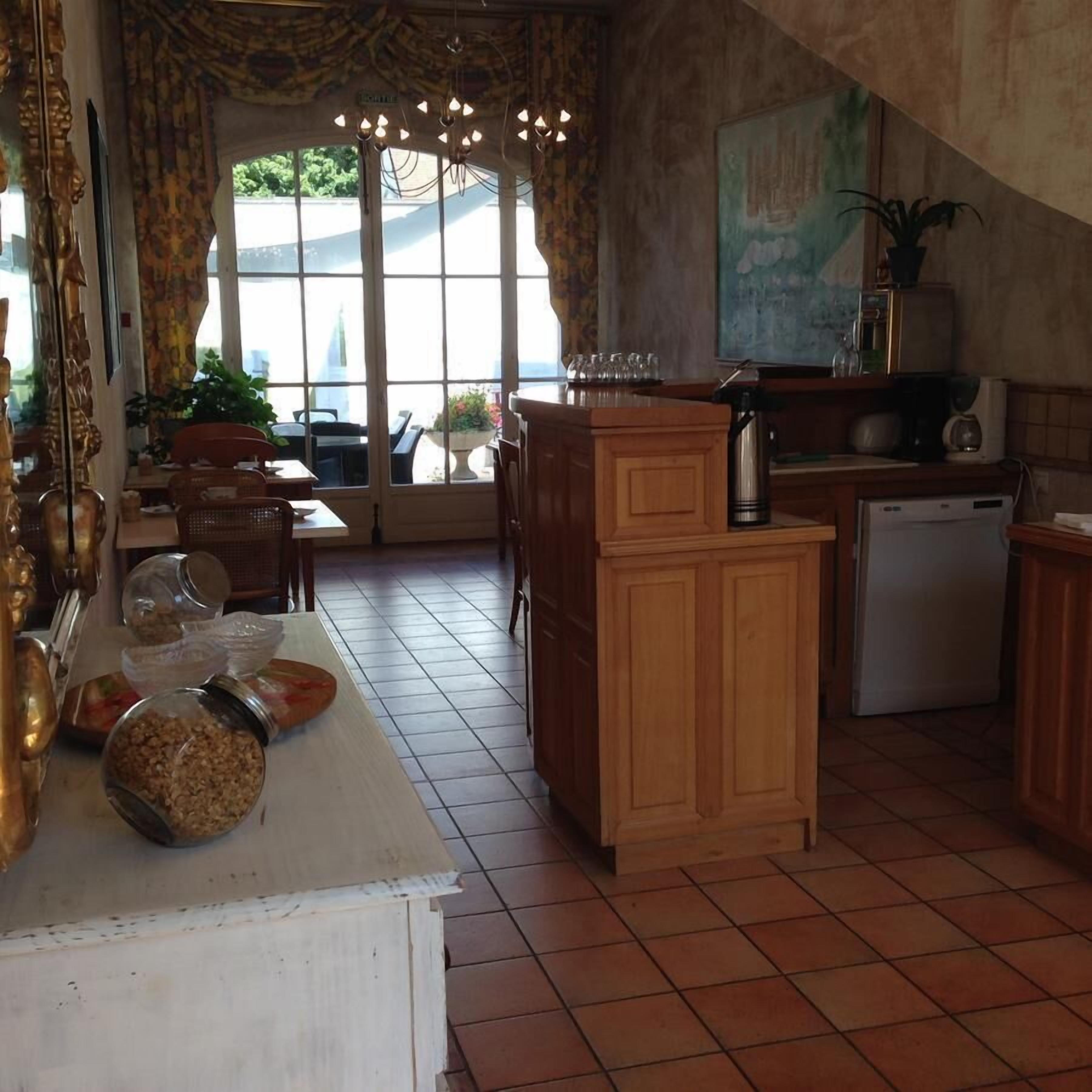 A kitchen with a wooden counter, a coffee machine, and a refrigerator. There are jars on the counter and a window with curtains.