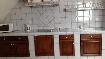 Una cocina con salpicadero de azulejos blancos, armarios de madera, microondas y cafetera.