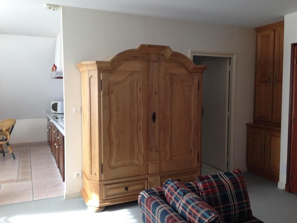 A room with a large wooden wardrobe, a sofa, and a chair.