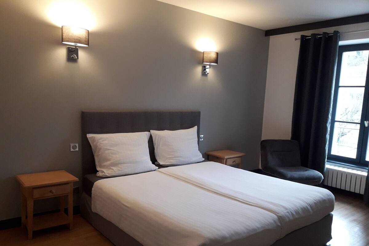 A hotel room with a large bed, two bedside tables, a chair, and two wall-mounted lights.