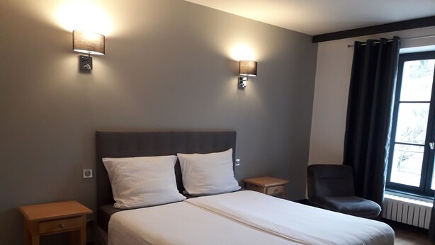 A hotel room with a large bed, two bedside tables, a chair, and two wall-mounted lights.
