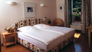 A bedroom with a large bed, wooden floor, two bedside tables, a chair, and a window with curtains.